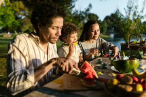 A cheerful family sharing a delightful picnic outdoors, enjoying watermelon on a sunny day.